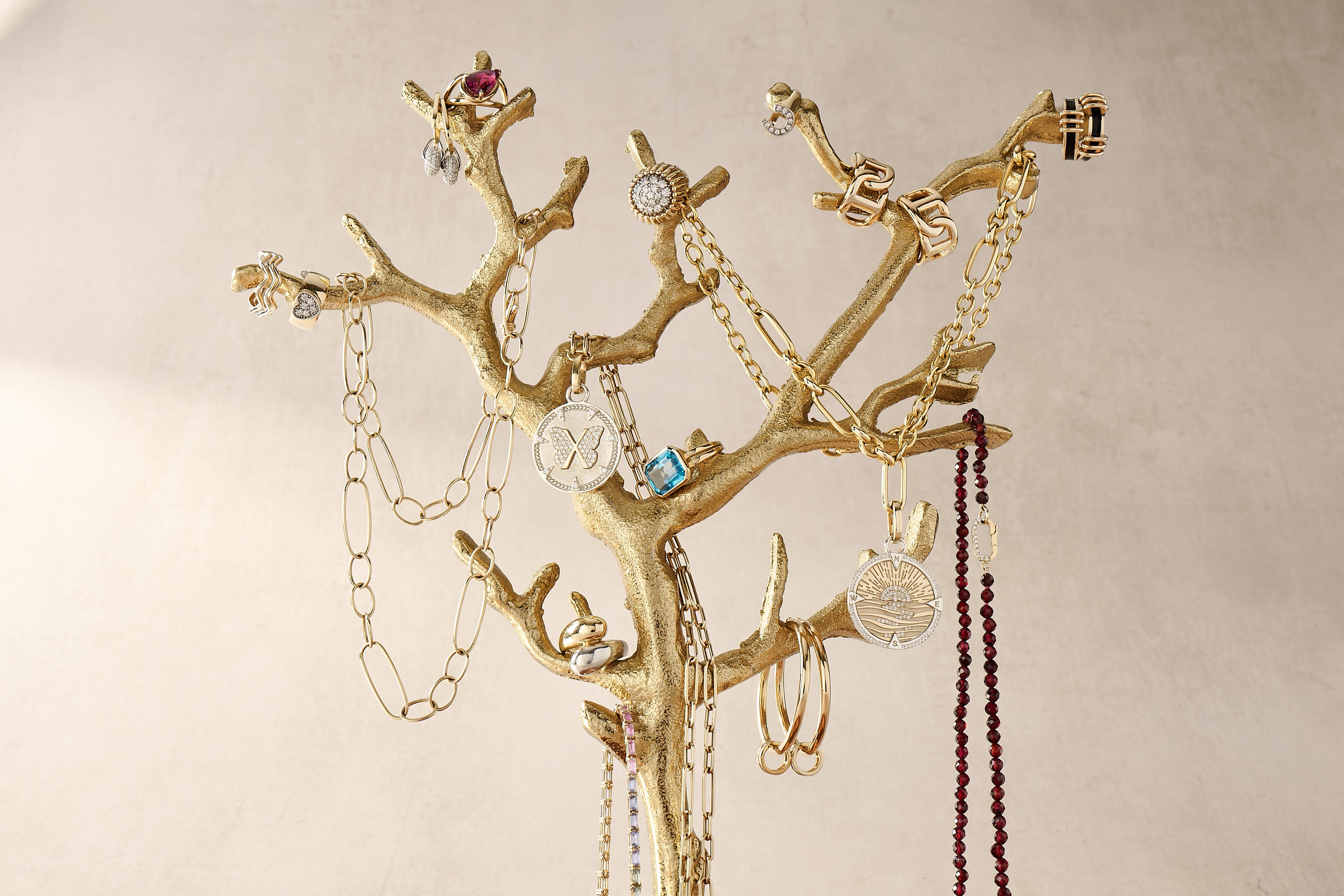 Gold jewelry tree with various necklaces and bracelets on a beige background