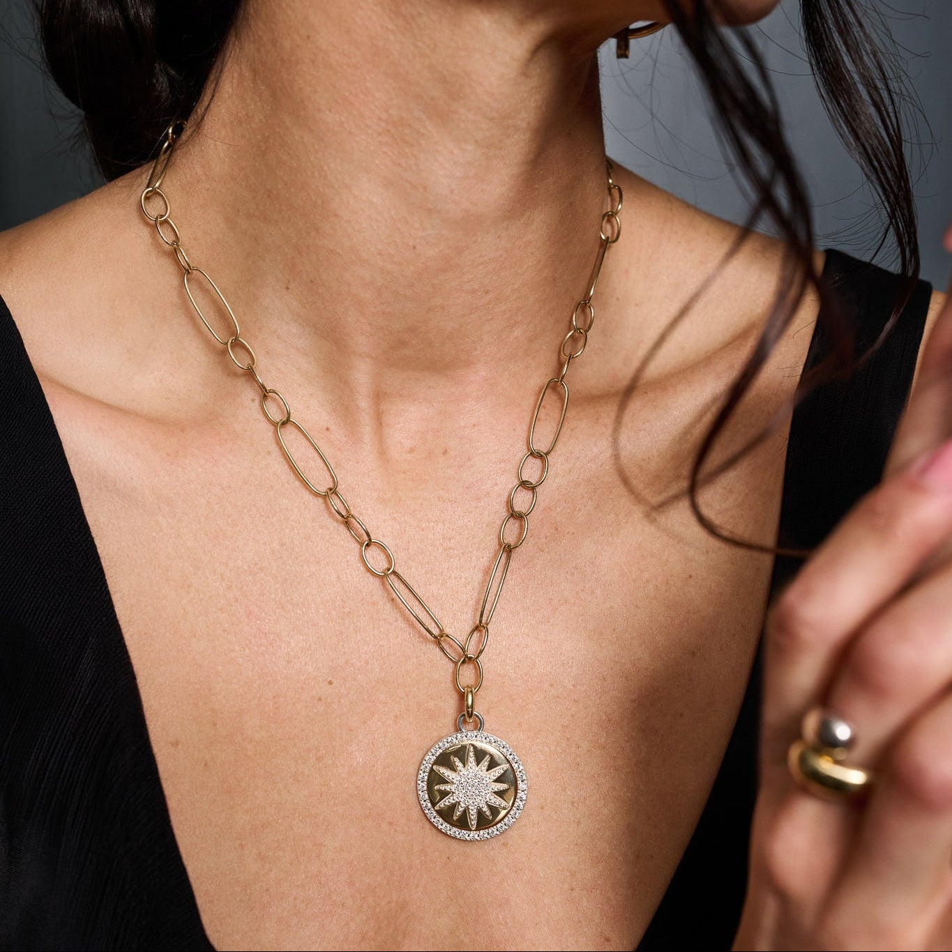 Gold chain necklace with a sun pendant worn by a person against a neutral background