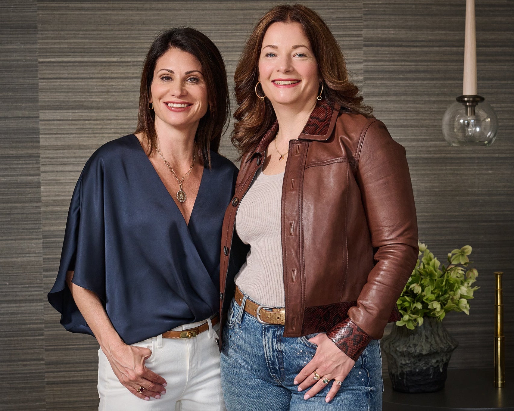 Two women standing side by side in a well-lit room with a decorative background.