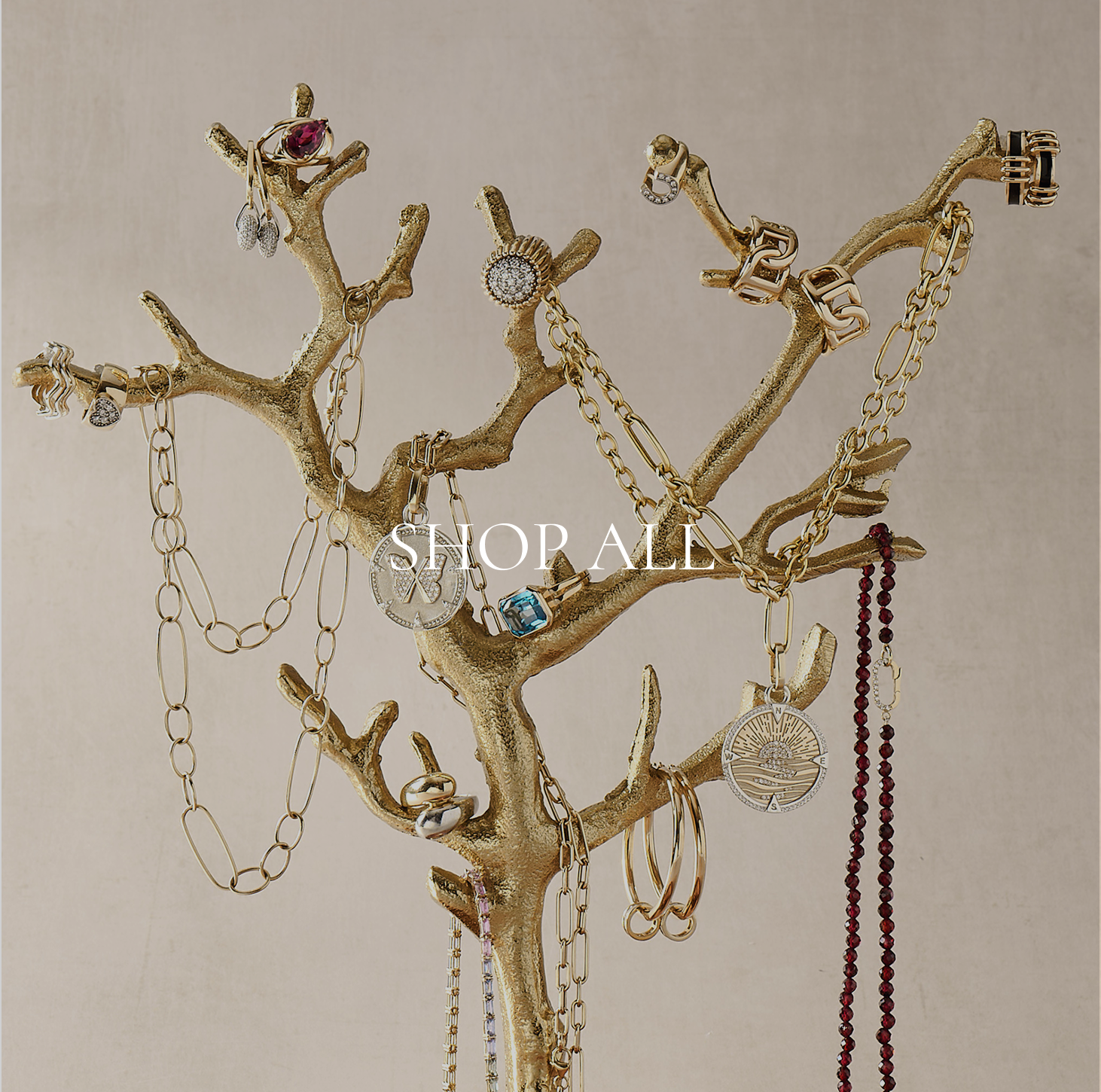 Gold jewelry tree with various pieces of jewelry on a beige background